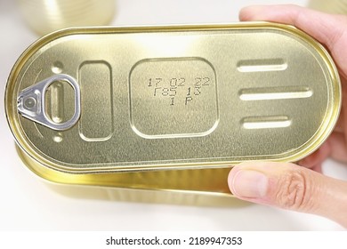 Hand Holds Sealed Tin Can On White Background. Canned Fish, Seafood In Tin Can. Close-up Tin Can. Food Storage. Simple And Cheap Food Concept. Seafood Preservation.