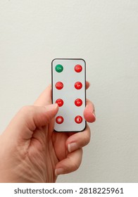 A hand holds a small, rectangular remote control with several red buttons and one green button.