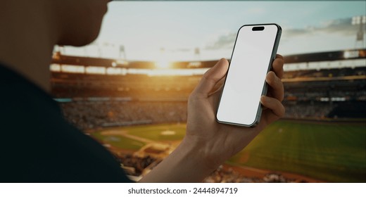 A hand holds a smartphone with a green screen at a baseball stadium, perfect for sports apps with live scoring, streaming, or fantasy league tracking - Powered by Shutterstock