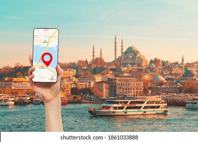A hand holds a smartphone with an online maps app. In the background, a river with a tourist ship. Istanbul, Turkey. Concept of travel, cruises and online applications