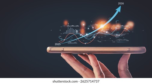 A hand holds a smartphone, upon which a glowing digital financial chart projects upward growth from 2025 to 2026.