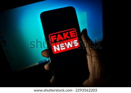 Hand holds a smartphone where the phrase fake news appears on the screen.

Image with news concept and low light