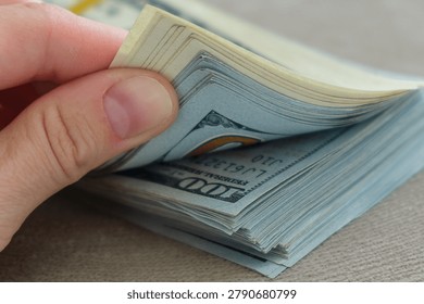 Hand holds stack of crisp U.S. Dollar bills. Fingers gently grip the topmost bill. Money appears fresh and well-organized. Close-up emphasizes value and financial success. Ideal for themes of earnings