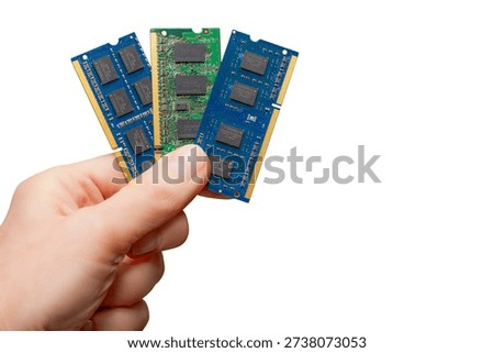 A hand holds three memory modules representing different types of DRAM memory. The lack of supply affects many devices and markets.
