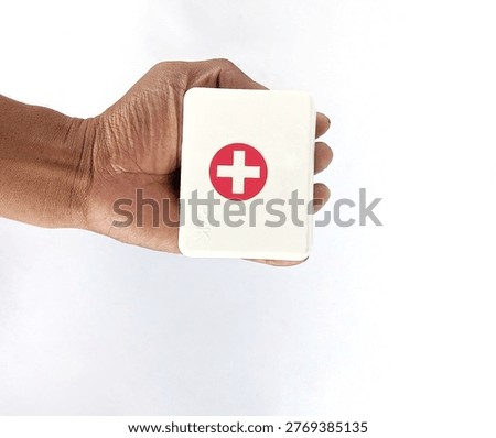 A hand holds a white rectangular box with a red cross emblem on the front against a plain white background.