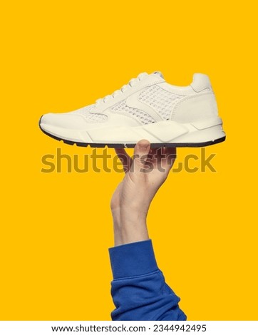 Hand holds white running sneaker on bright yellow background with copy space. Close up. Outlet marketing poster