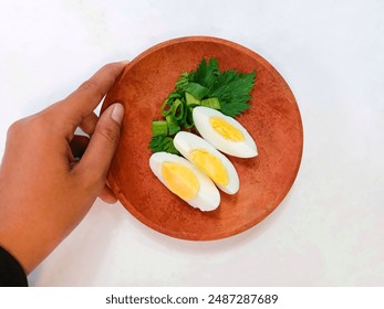 a hand holds a wooden plate containing pieces of boiled chicken eggs and leek on a white background. healthy food and protein boiled eggs. three pieces of boiled eggs. egg white and yolk. top view - Powered by Shutterstock