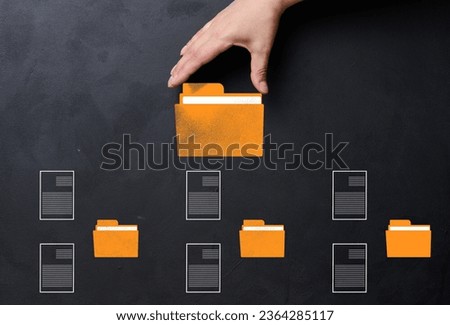 A hand holds a yellow folder over a black background with several folders and documents scattered around. Concept of control and systematization of documents
