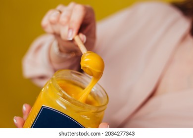 A hand and honey spoon draws out the sticky contents  Yellow honey stretches in glass jar 