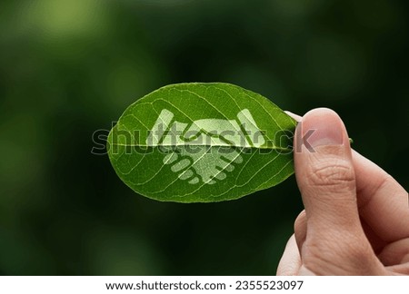 Hand of human is holding painted green leaf with handshake icon, environment social and governance or ESG, Cooperation of organization for prevent climate change  sustainable earth. [[stock_photo]] © 