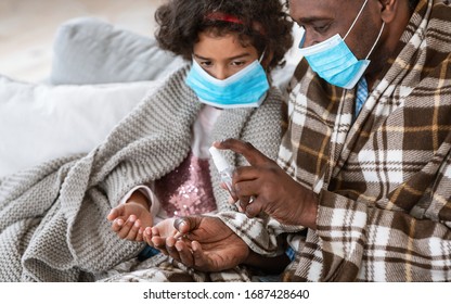 Hand Hygiene During Pandemic. African American Man And His Granddaughter With Masks Applying Antiseptic At Home