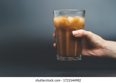 Hand with ice coffee in a tall glass on dark background. - Shutterstock ID 1721544982