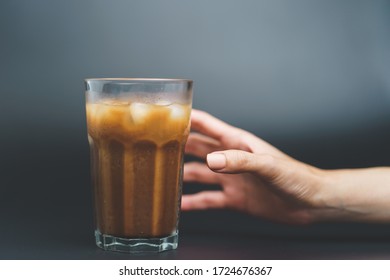 Hand with ice coffee in a tall glass on dark background. - Shutterstock ID 1724676367