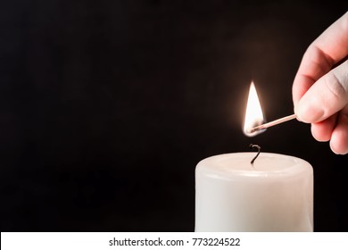 Hand ignite a white candle with match stick on the dark background. Condolence and religion concept. Empty place for a text.
