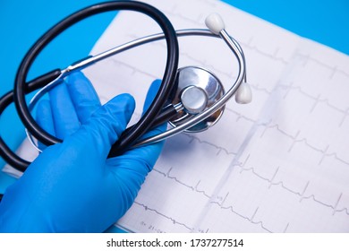 Hand Inblue Glove Holding Stethoscope Over Ecg Strip On Blue Background, Selective Focus.