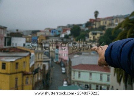 A hand with the index finger extended pointing towards the city of Valparaíso, renowned for its coastal charm, colorful houses on the hills, and vibrant port culture in the central region of Chile.
