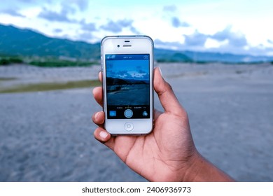 Hand of a Indonesian Man Holding an Old Iphone 5 on Sand Dune or Gumuk Pasir on Cloudy Day at Depok Beach Bantul Yogyakarta Indonesia