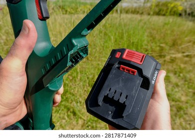 Hand inserting a 4Ah rechargeable lithium battery into a cordless garden power tool for longer runtime outdoors.