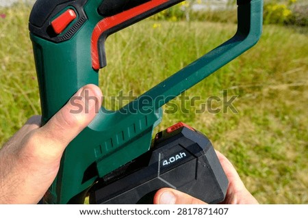 Hand inserting a 4Ah rechargeable lithium battery into a cordless garden power tool for longer runtime outdoors.
