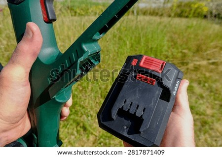 Hand inserting a 4Ah rechargeable lithium battery into a cordless garden power tool for longer runtime outdoors.
