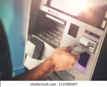 Man’s hand inserting ATM credit card into bank machine to transfer money or withdraw