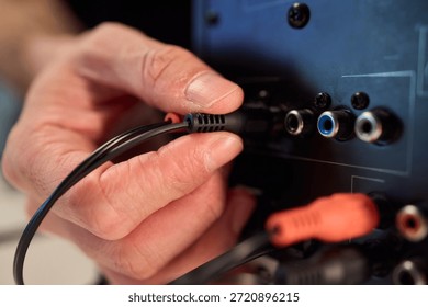 Hand inserting audio plug into subwoofer back panel during stage soundcheck, closeup of fingers holding metal connector, textured cabinet surface, focused