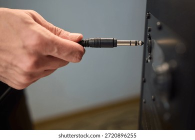 Hand inserting audio plug into subwoofer back panel during stage soundcheck, closeup of fingers holding metal connector, textured cabinet surface, focused