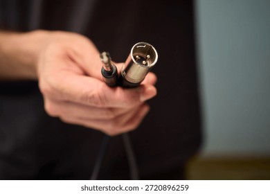 Hand inserting audio plug into subwoofer back panel during stage soundcheck, closeup of fingers holding metal connector, textured cabinet surface, focused