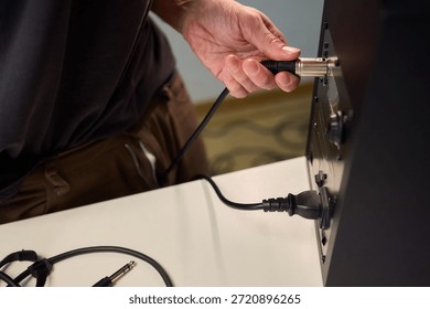 Hand inserting audio plug into subwoofer back panel during stage soundcheck, closeup of fingers holding metal connector, textured cabinet surface, focused