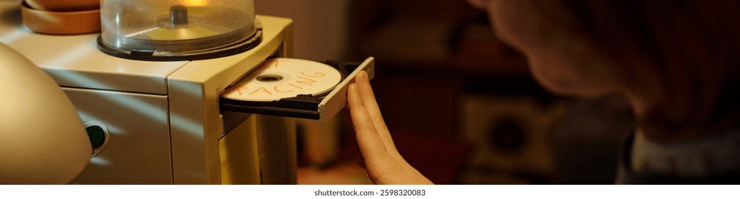 Hand inserting CD labeled RACING into a sleek modern CD drive with a warm ambient lighting