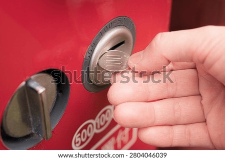 Hand inserting coin into a silver slot on a red vending machine closeup view