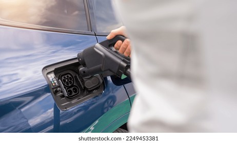 Hand inserting a DC CCS2 EV charging connector into electric car socket at charging station, Hypercharger or Supercharger.  Charge electromobility concept image.