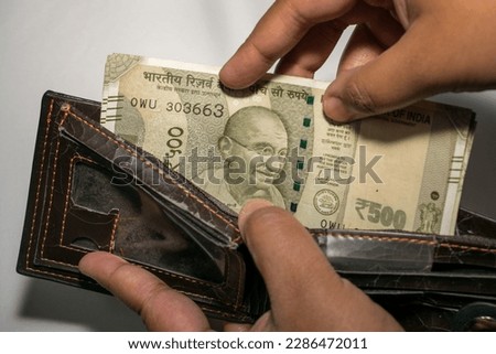 A hand inserting five hundred rupee Indian banknotes in a wallet on a white background