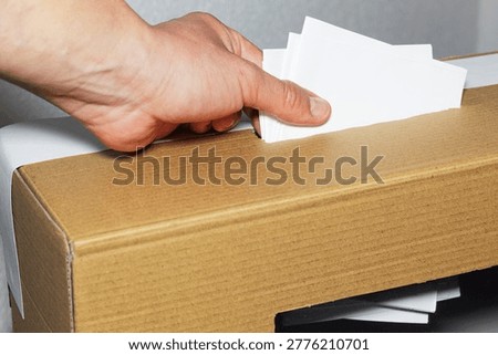 A hand inserting multiple ballots into a ballot box, manual voting and electoral crime