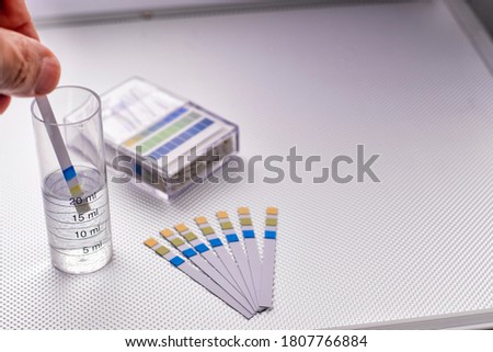hand inserting a ph control strip into a graduated cylinder with water, selective focus