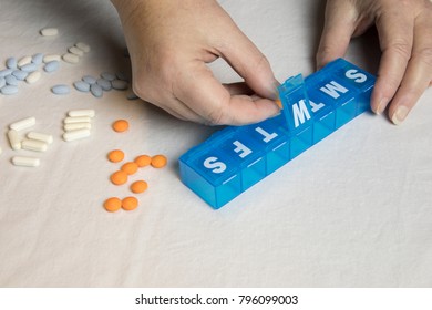 Hand Inserting Pills Into Blue Plastic Pill Weekly Organizer On White.