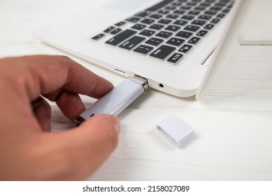 Hand inserting a USB flash drive into a laptop on a white background. Close-up of woman's hand plug USB flash drive on laptop at home. Copying data from a flash drive to a laptop