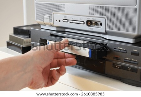 Hand inserting a VHS tape into a video cassette player at home