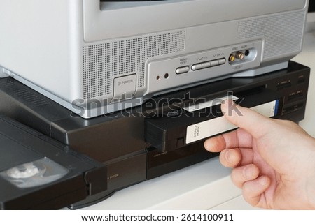Hand inserting a VHS tape into a video cassette player at home