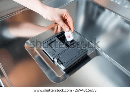 Hand inserts dishwasher detergent tablet into dispenser - tablet, detergent, dishwasher, clean, cycle.