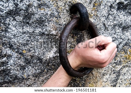 A hand inside a round iron circle attached to a stone wall.
