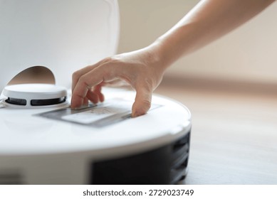 A hand interacting with the control panel of a smart robotic vacuum cleaner