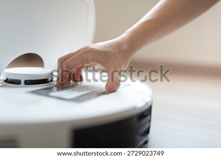 A hand interacting with the control panel of a smart robotic vacuum cleaner