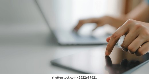 Hand Interacting with Tablet Screen While Using Laptop in Background. Digital Multitasking, Remote Work, and Modern Technology. Concept of Online Productivity and Interactive Business Solutions.