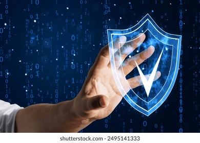 Hand interacting with a virtual shield featuring a check mark, surrounded by binary code on a dark blue background. Concept of digital security and data protection