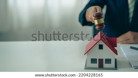 Hand of a judge holding a hammer and a house model mediating property disputes in court or property auctioneers with the god of justice on the table.