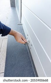 Hand With A Key Closing A Roller Shutter Door Of A Store. Closing Concept