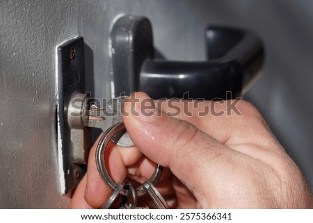 hand with keys, entering lock, black knob, on a white door with shadow, and side view