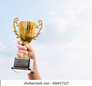 Hand Of Kid Holding The Golden Trophy Cup And Sky Background