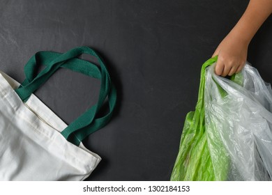 Hand Kid Holding Plastic Bags And Canvas Tote Bag On Black Stone Background, Waste And Recycle Concept